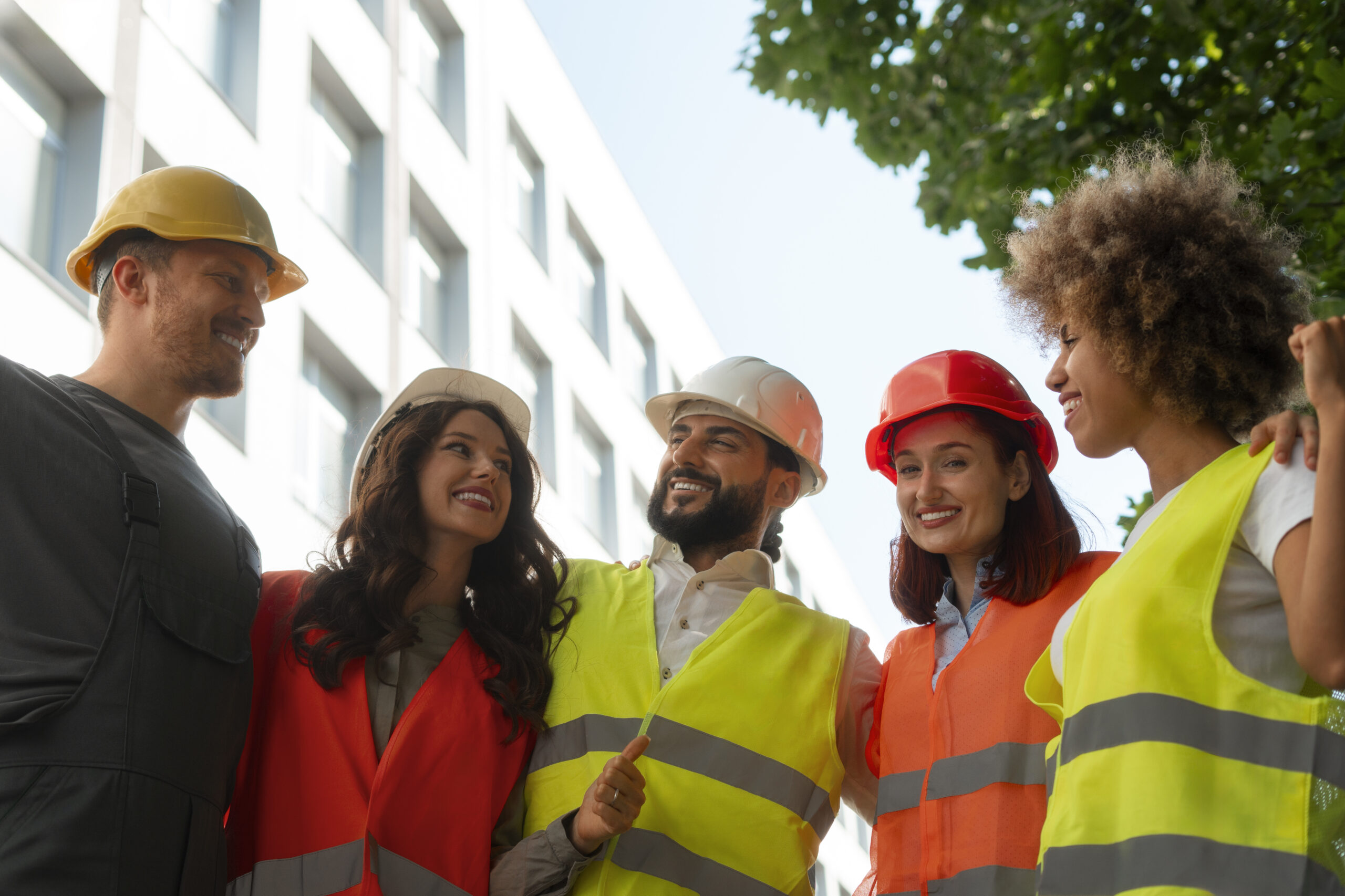 COURSES 10 Five construction workers wearing helmets and reflective vests stand together outdoors near a building.